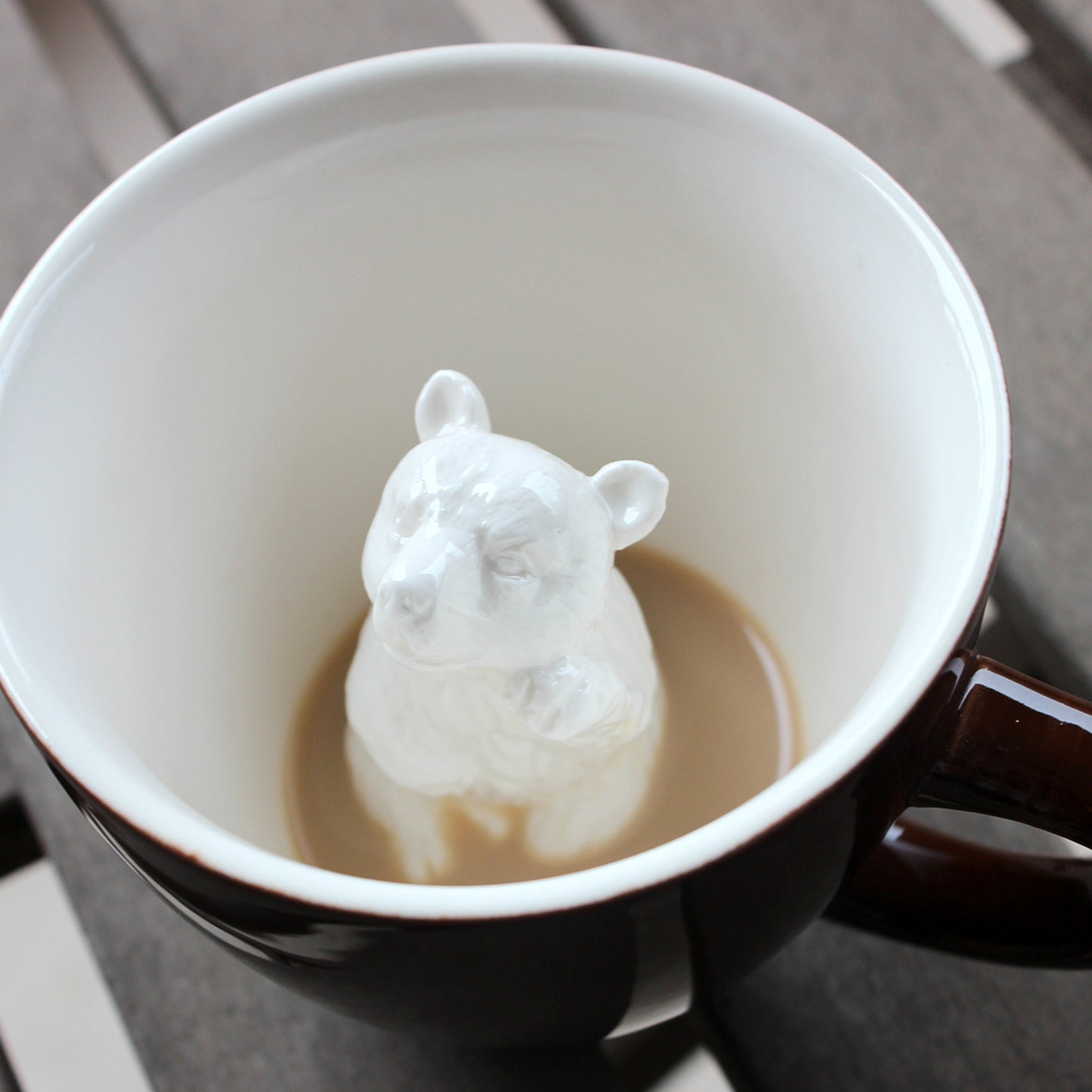 Dark brown bear Creature Cup partially submerged in coffee on top of a picnic table