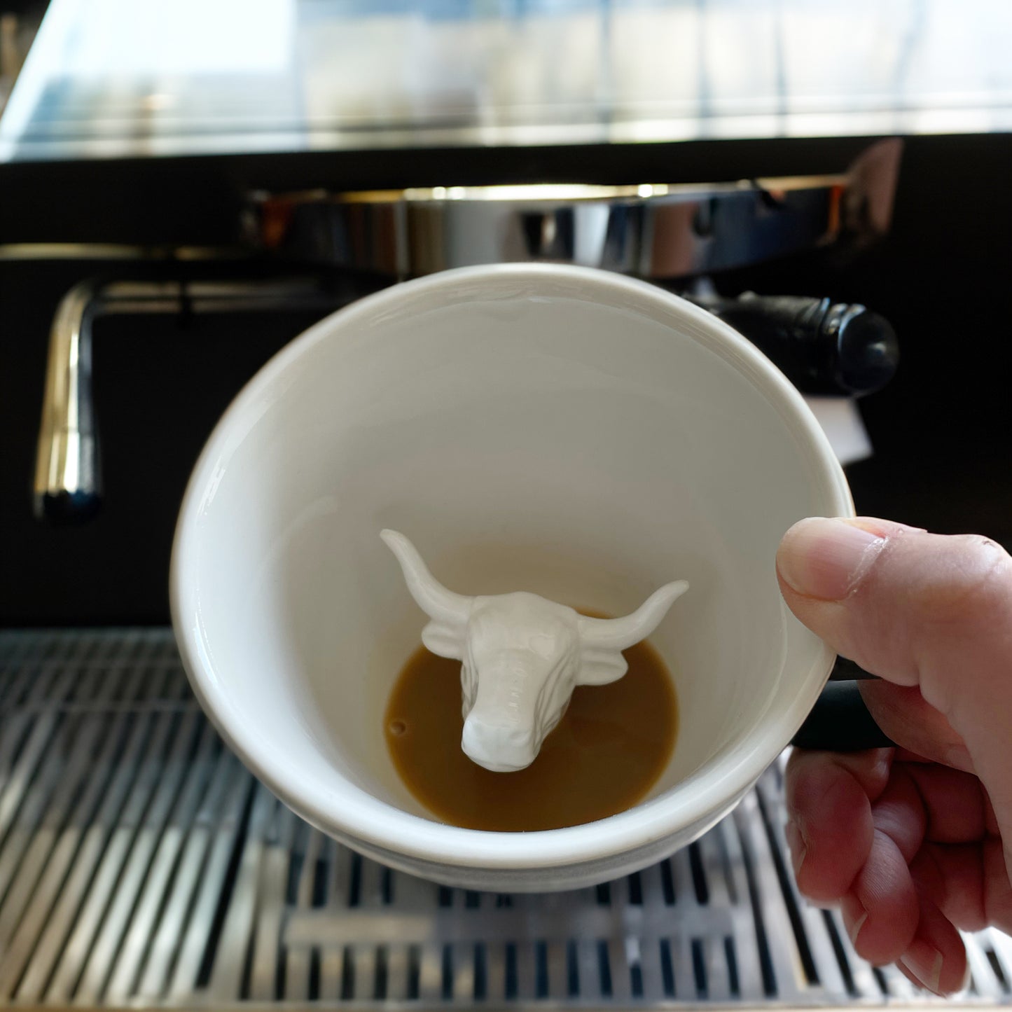 Matte olive brown bull Creature Cup partially submerged interior being held in front of an espresso machine