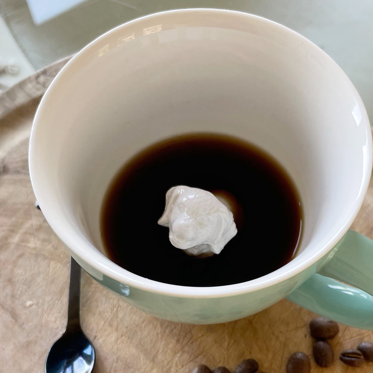 Aqua green Retriever Dog Creature Cup interior partially submerged on a cutting board with coffee beans and a spoon nearby