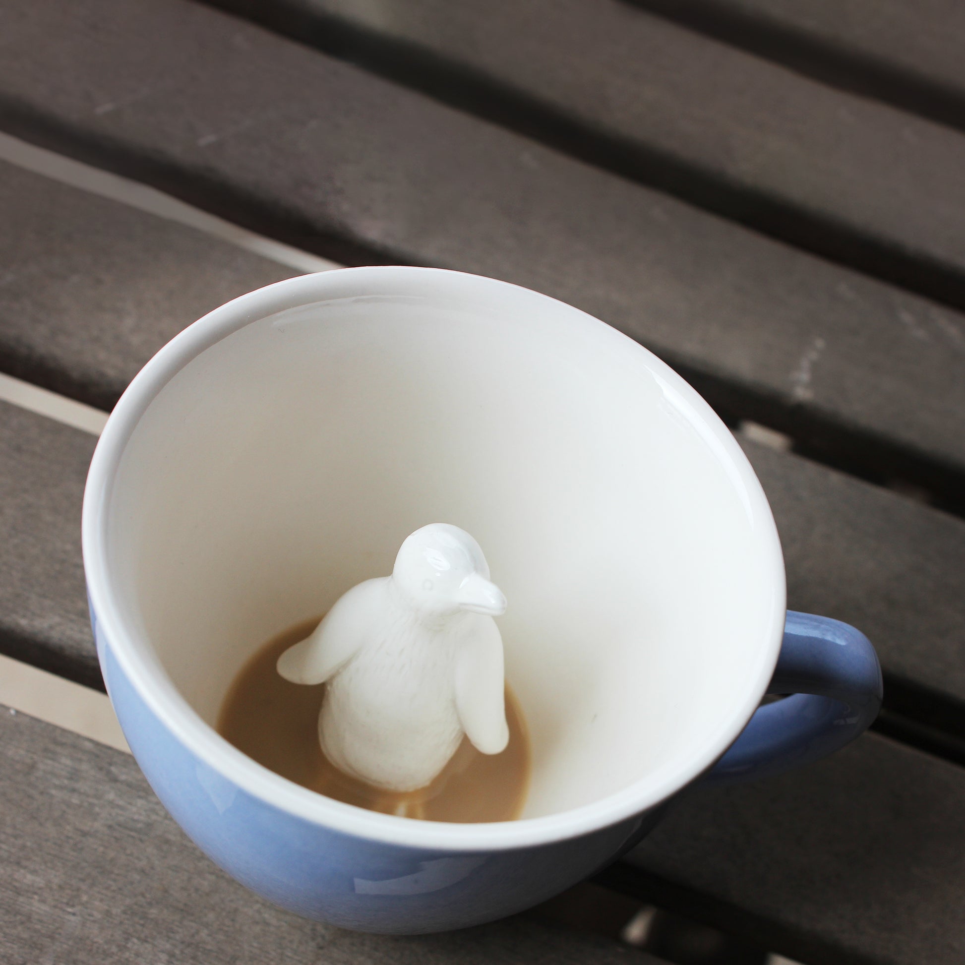 Penguin Ice blue Creature Cup partially submerged on a wooden table