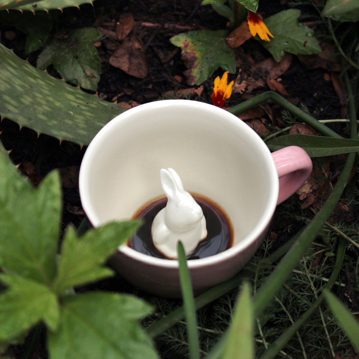 Blush pink rabbit Creature Cup sitting in a patch of brush