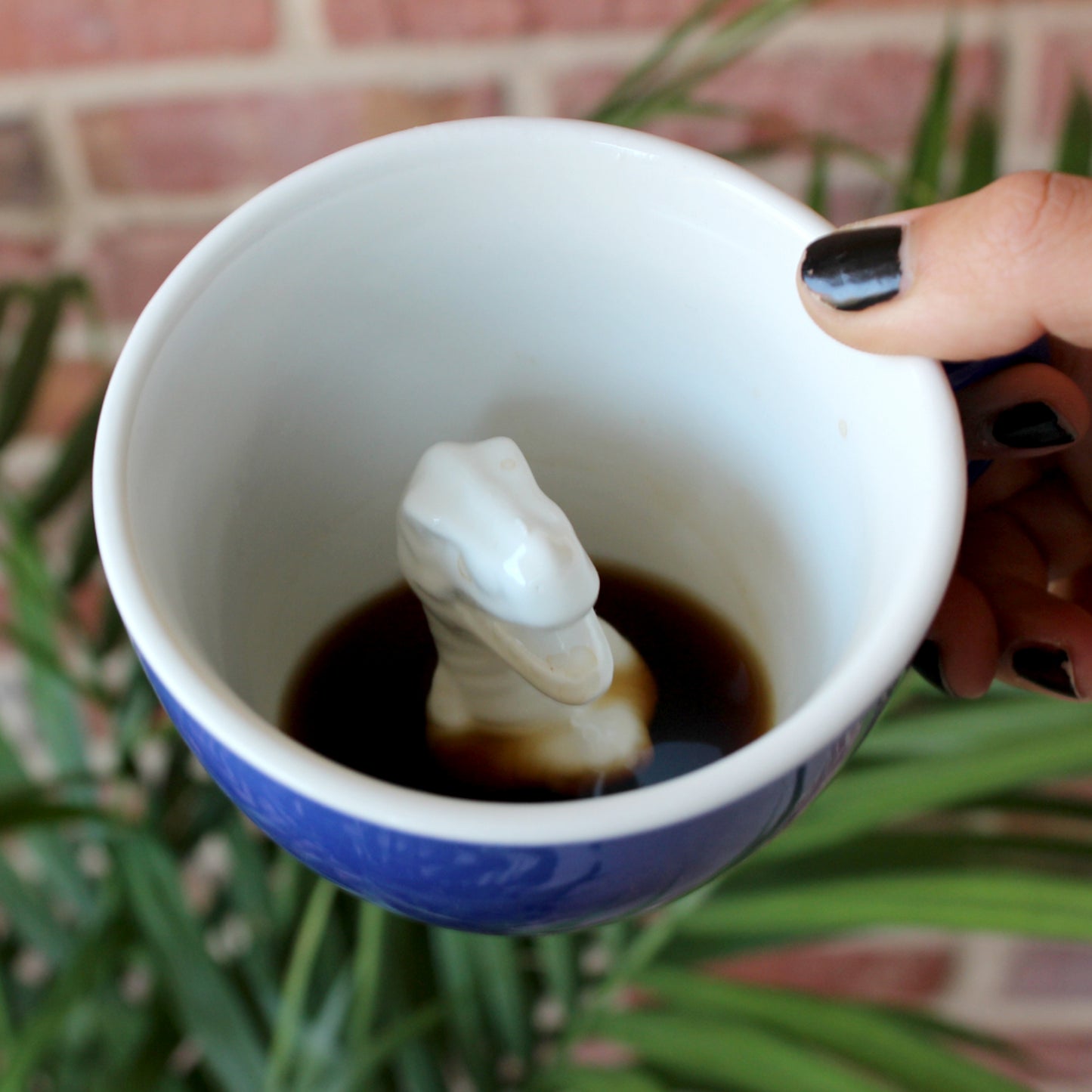 Cobalt blue T-Rex Creature Cup partially submerged interior held in front of a plant and brick wall