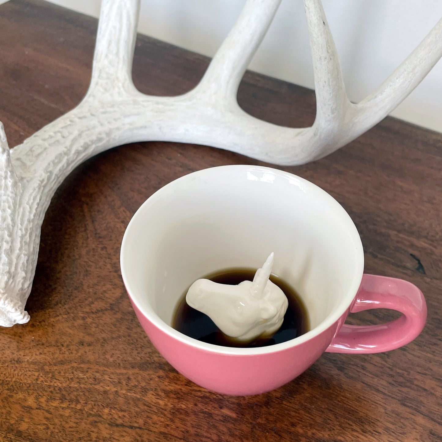 Bubblegum pink Unicorn Creature Cup partially submerged on a tabletop with an antler in the background