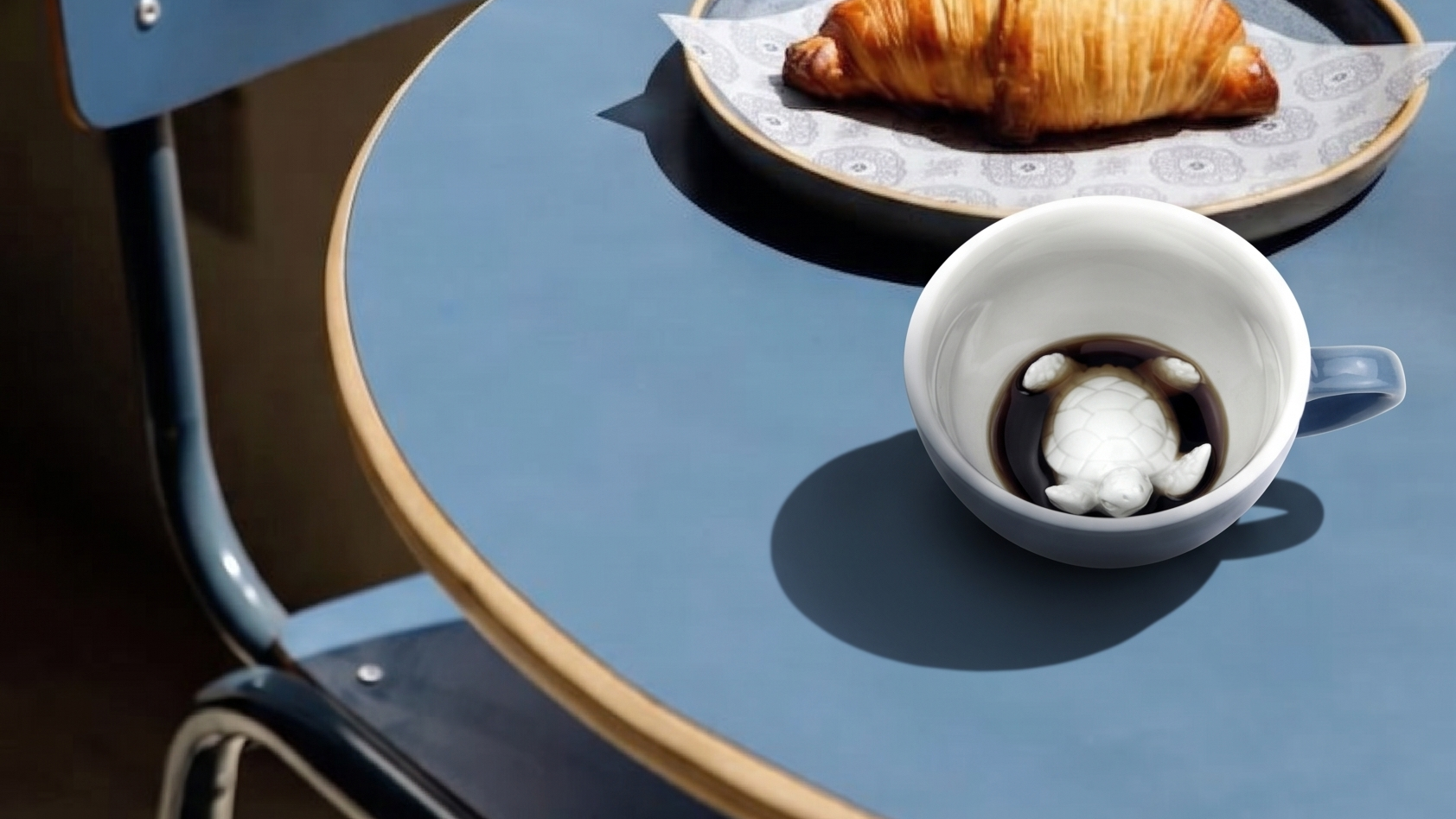 Blue chair with a plate of croissant and creature coffee cup on a matching table.